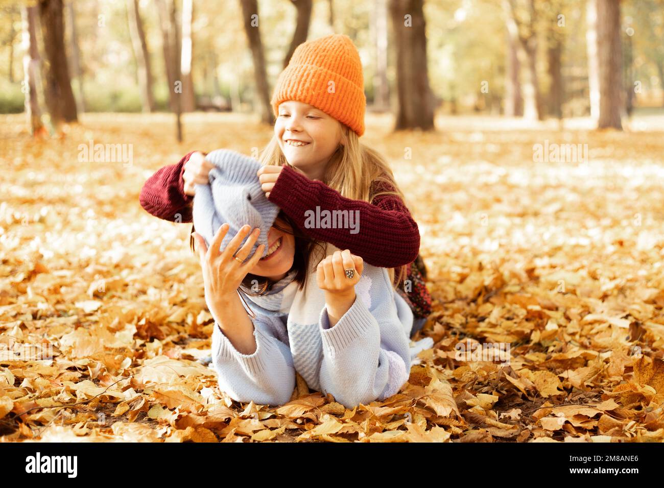Portrait of family of young woman and teenage girl lying on yellow fallen leaves in forest park in autumn, having fun. Stock Photo