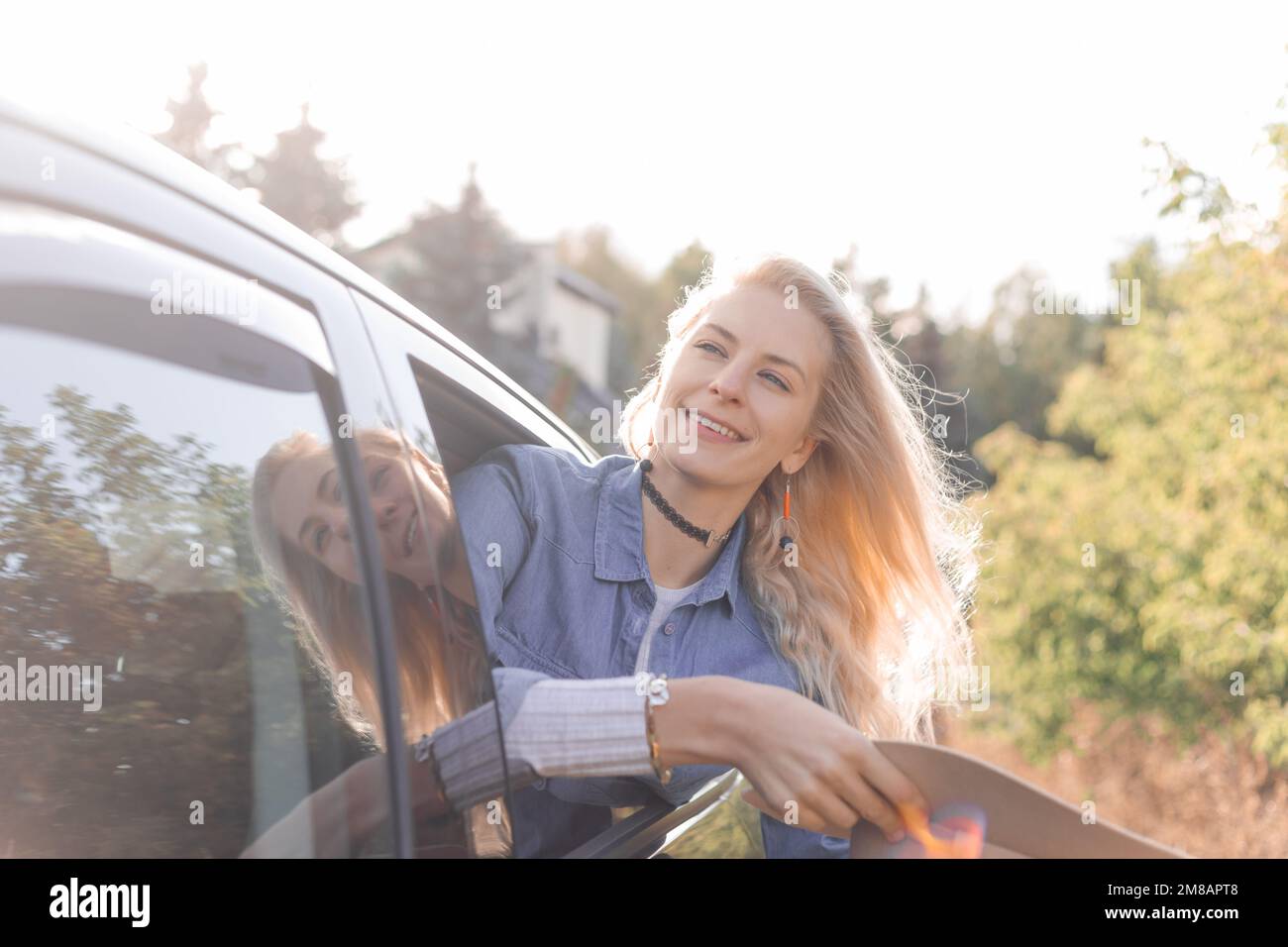 Glad, pensive, smiling, proud blond woman hold hat in hands, leaning out of car window on backseat. Journey, travelling Stock Photo