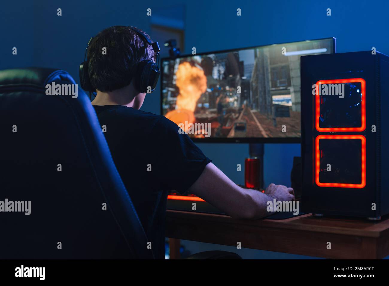 Young professional gamer playing tournaments online video games on computer with headphones in his room, red and blue neon color