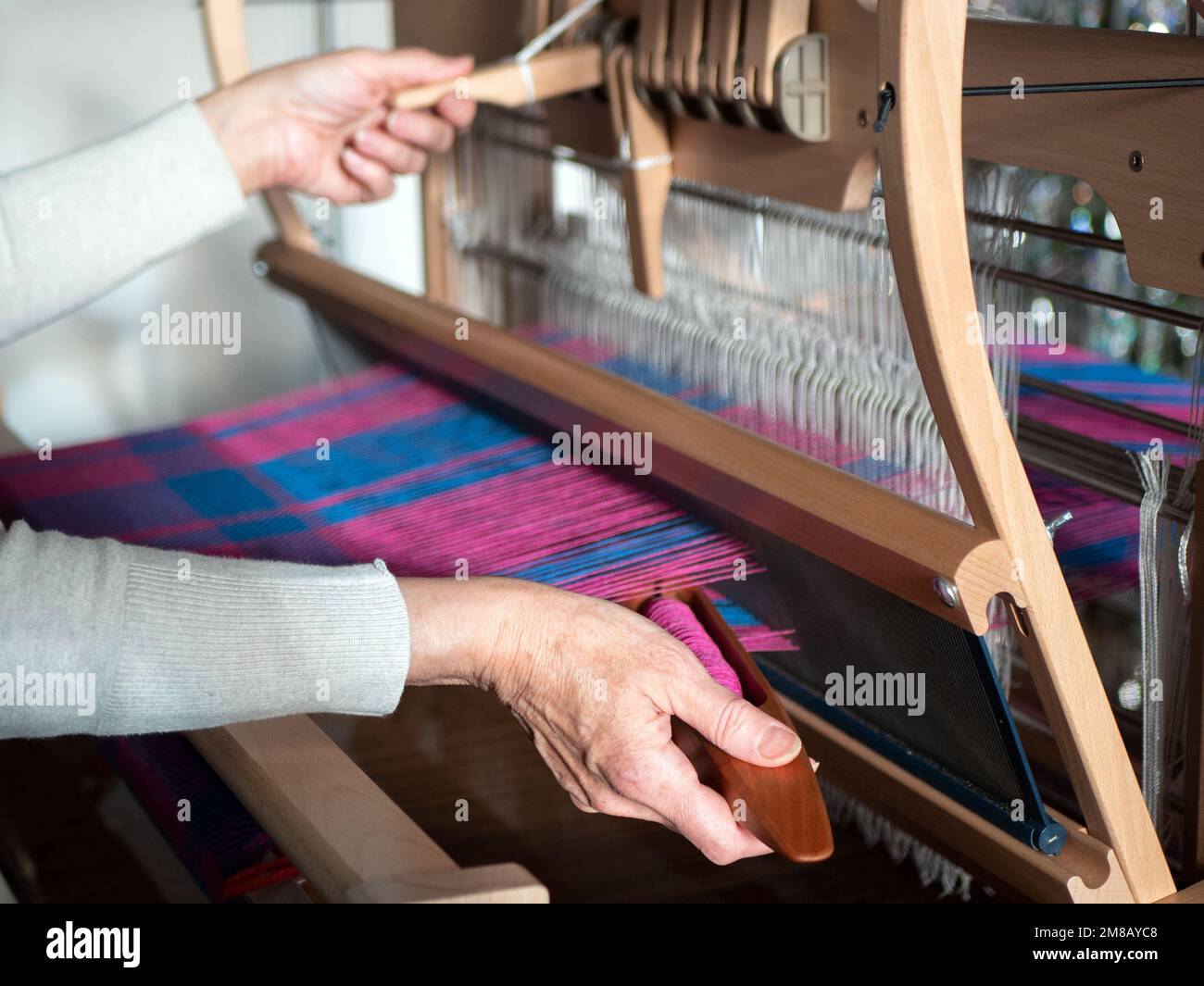 Weaving process using table loom made of wood, selective focus. Woman