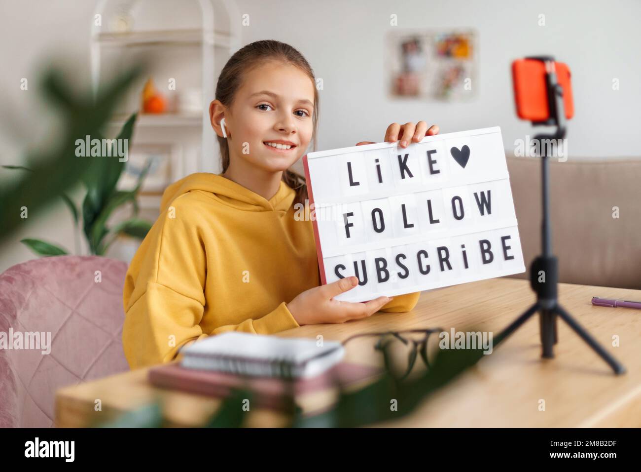 Confident girl blogger sitting at desk at home and shooting live broadcast vlog on smartphone. Happy Caucasian vlogger influencer recording video blog on cellphone web camera. Communication concept Stock Photo