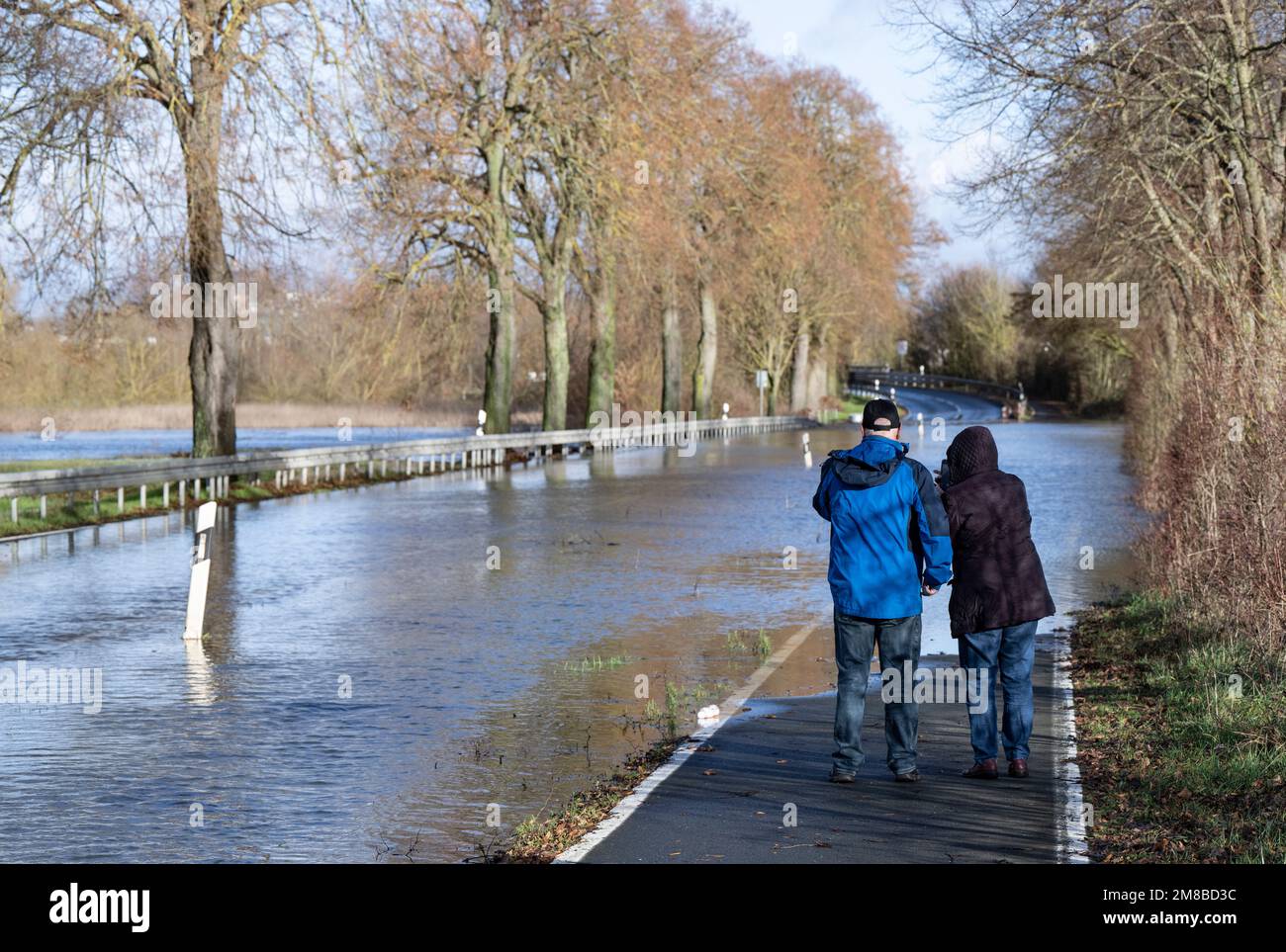 Heuchelheim, Germany. 13th Jan, 2023. Two walkers stand on a flooded country road near Heuchelheim in Hesse. Further rainfall could cause more rivers and streams to burst their banks. Credit: Boris Roessler/dpa/Alamy Live News Stock Photo