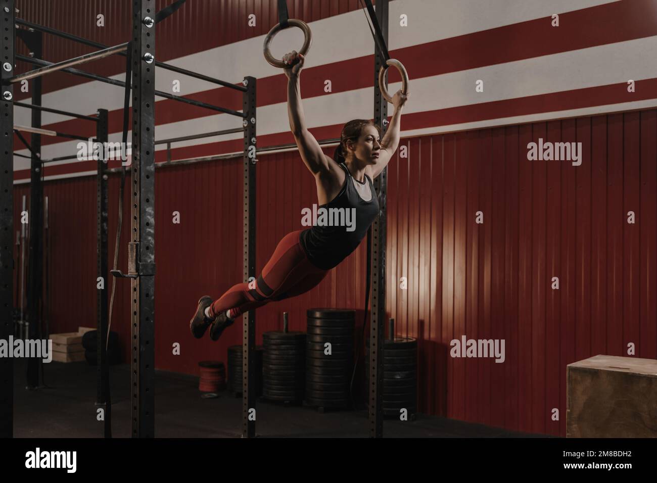 Young crossfit woman swinging on gymnastic rings. Female athlete doing muscle-ups exercise on rings at the gym. Sport motivation concept. Copy space Stock Photo