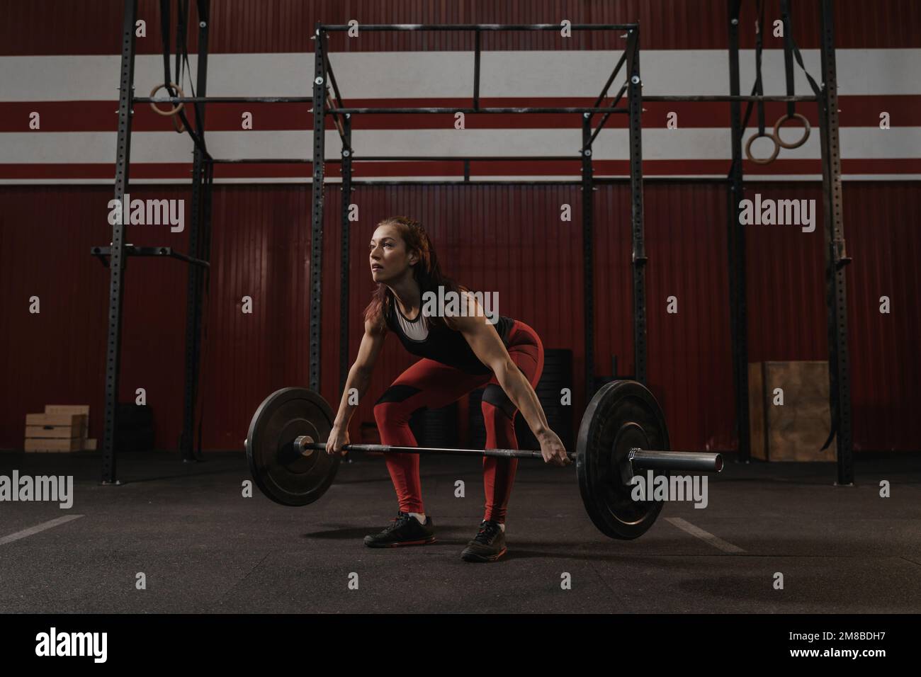Young female athlete doing deadlift exercise. Strong woman lifting heavy barbell at crossfit gym