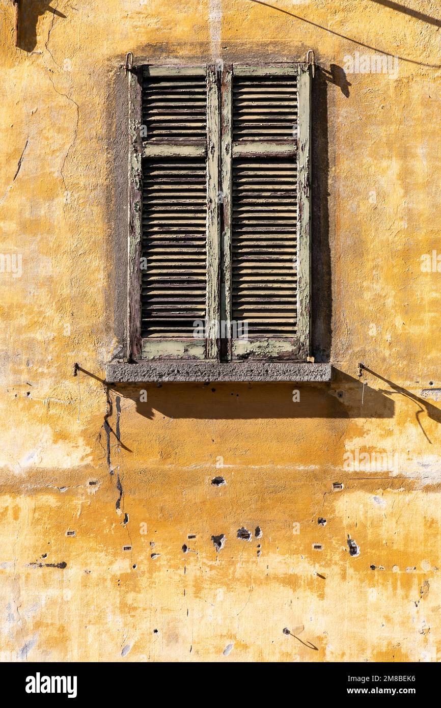 rustic old louvred window shutters set in a pockmarked yellow wall in bright sunshine Stock Photo