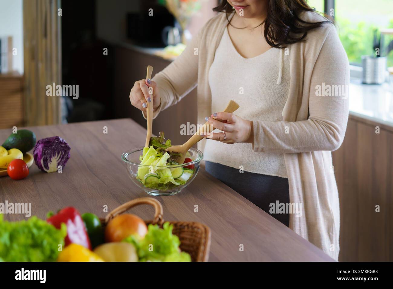 Beautiful Asian Pregnant Woman Happily Preparing a Vegetable Salad, Organic Healthy Food, in a Cozy Home Kitchen. Stock Photo