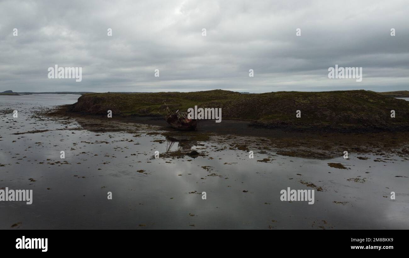 A landscape scene of a broken ship on the green hill island with gray ...