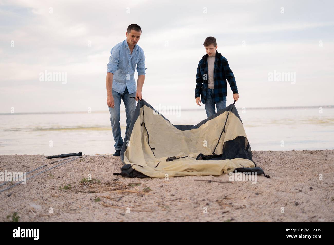 Father and son installing tent on river glade.Trekking with kids concept image. family spending time on nature. copy space Stock Photo