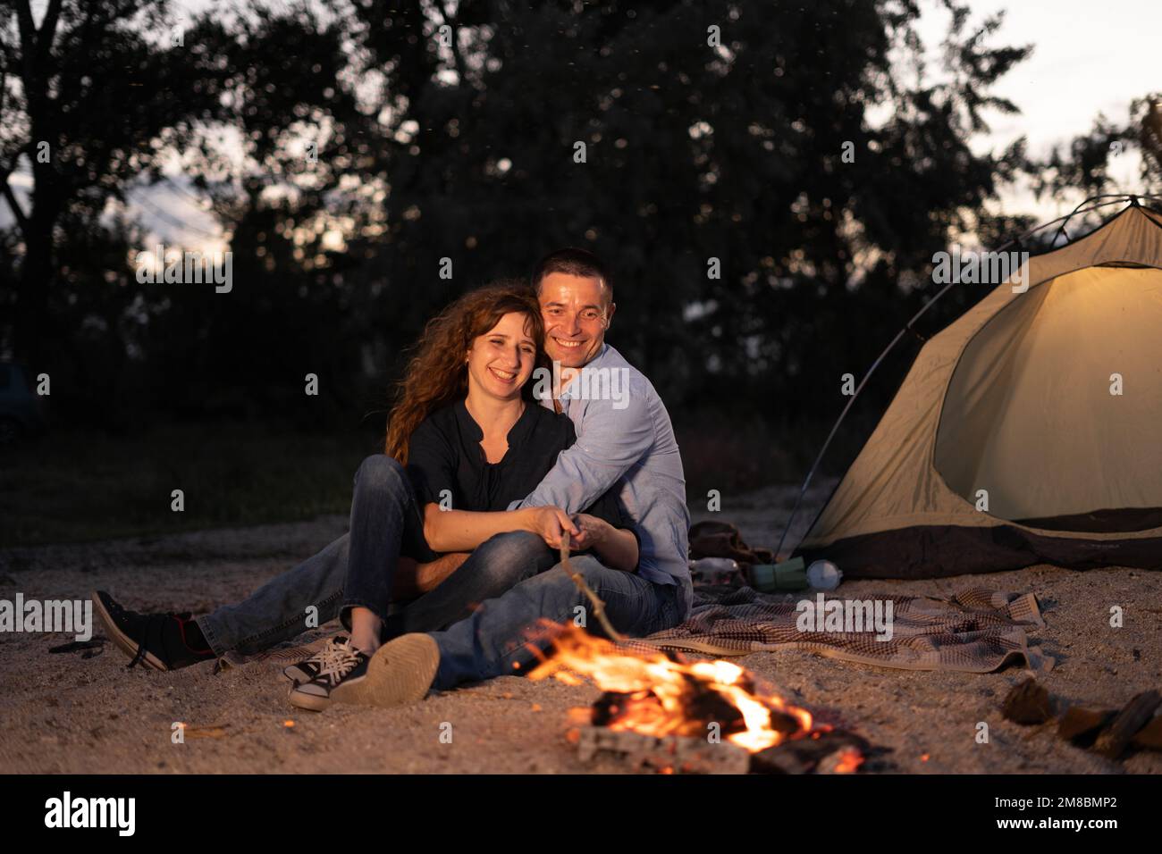 Man and woman tourists sitting in front of tent at campfire and forest ...