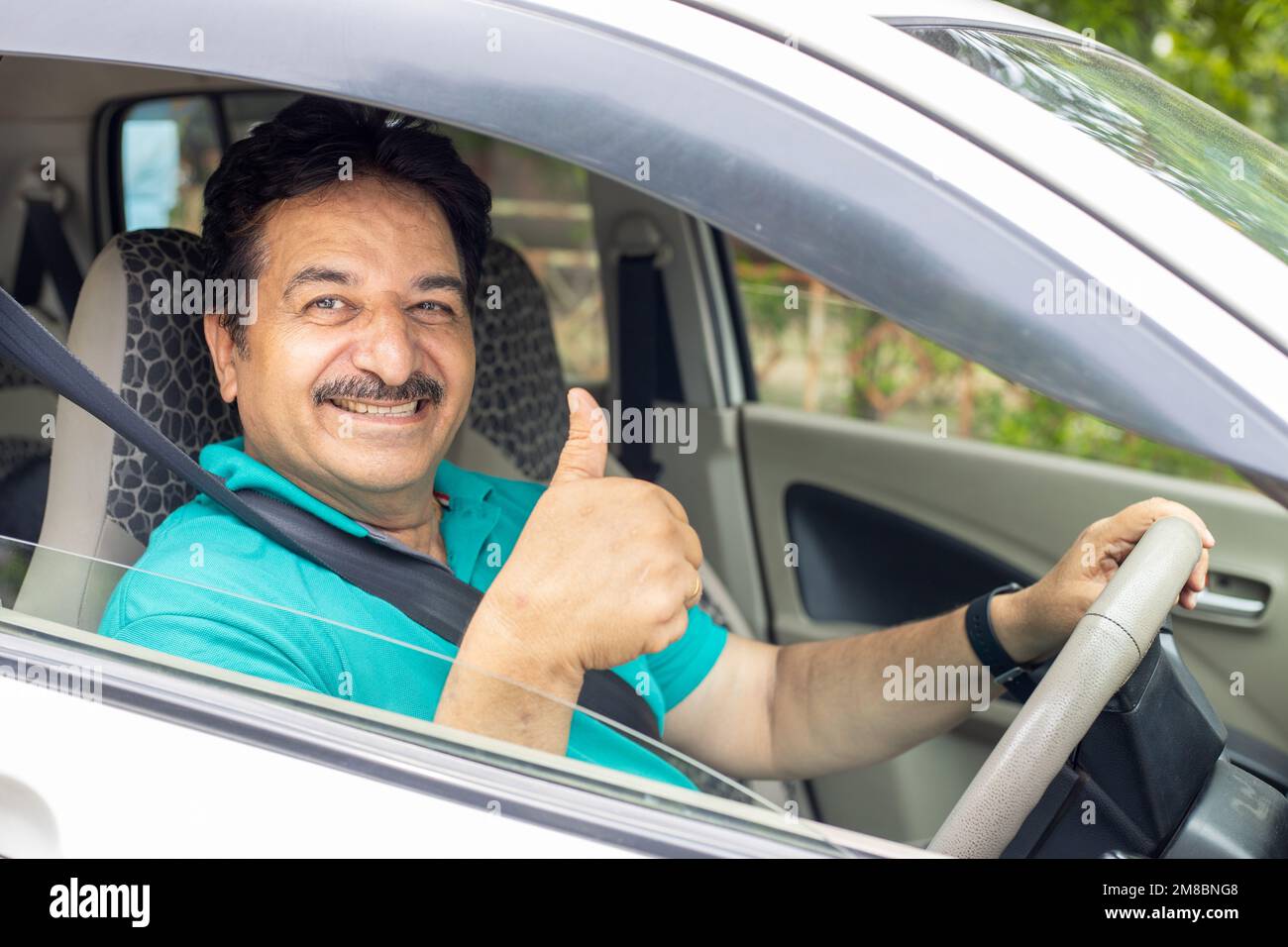 Happy indian mature man sitting in car wearing seat belt do thumbs up with hand ready to drive. Safety and people concept. Stock Photo