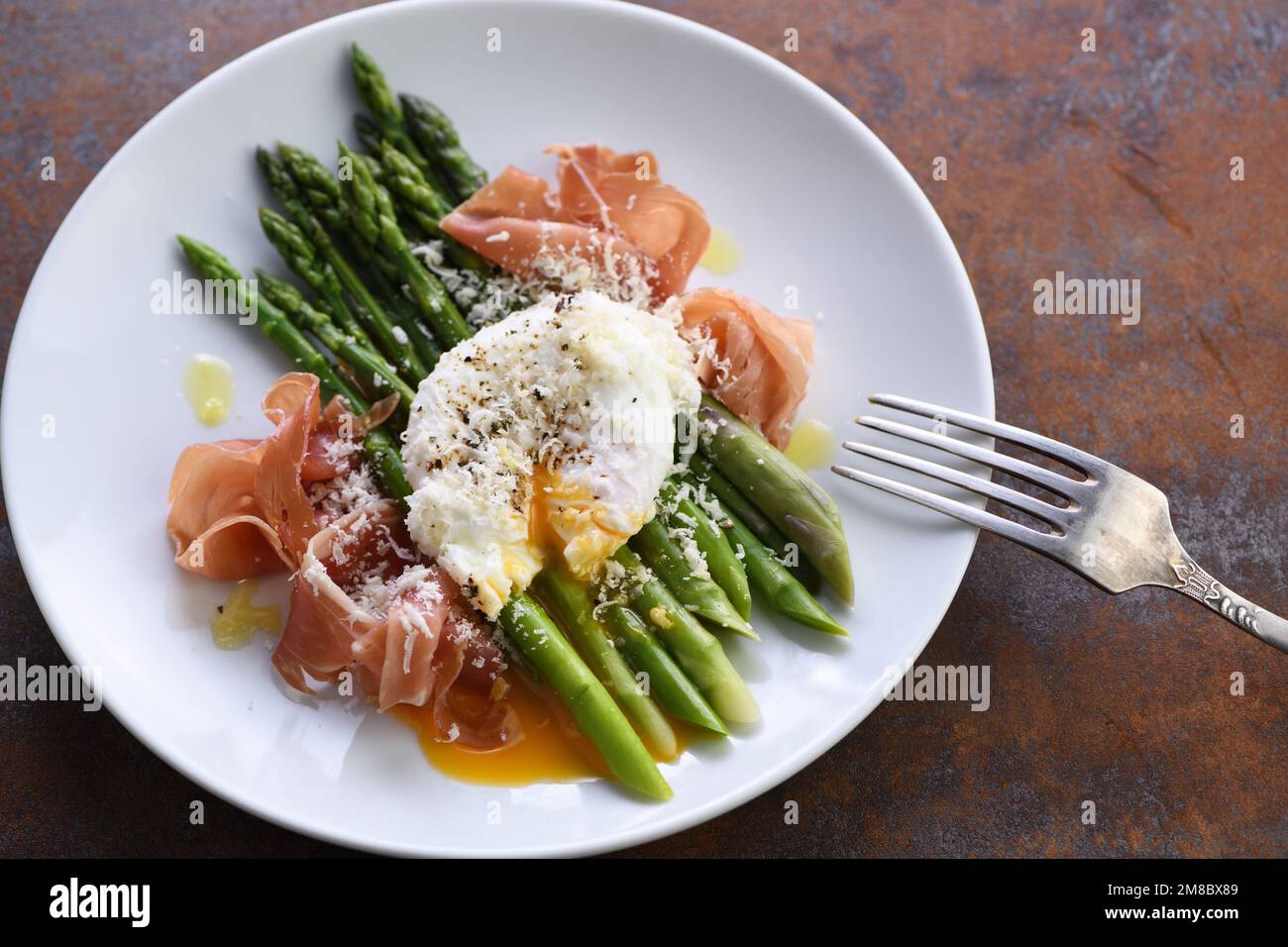 Eggs Benedict with parmesan, green asparagus and Parma ham Stock Photo