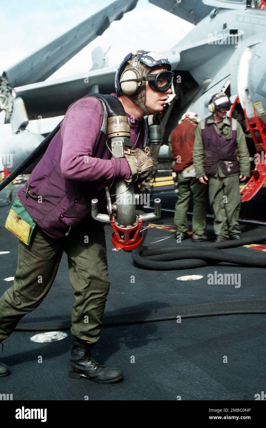 An aviation fuels crew member pulls a refueling line toward an aircraft