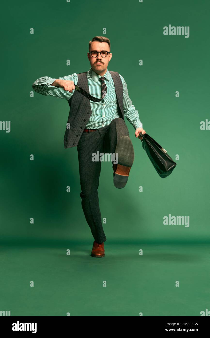 Motivation. Portrait of handsome man, businessman in classical suit with briefcase over green studio background. Concept of emotions, occupation Stock Photo