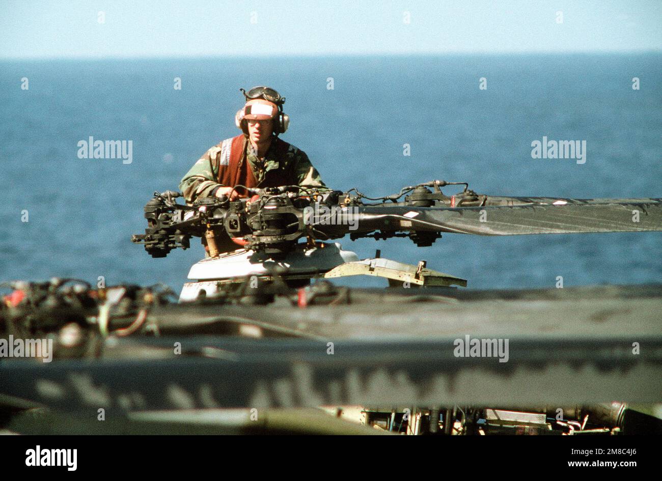 A flight deck crewman services the rotor hub of a helicopter during PACEX '89. Subject Operation/Series: PACEX '89 Country: Unknown Stock Photo
