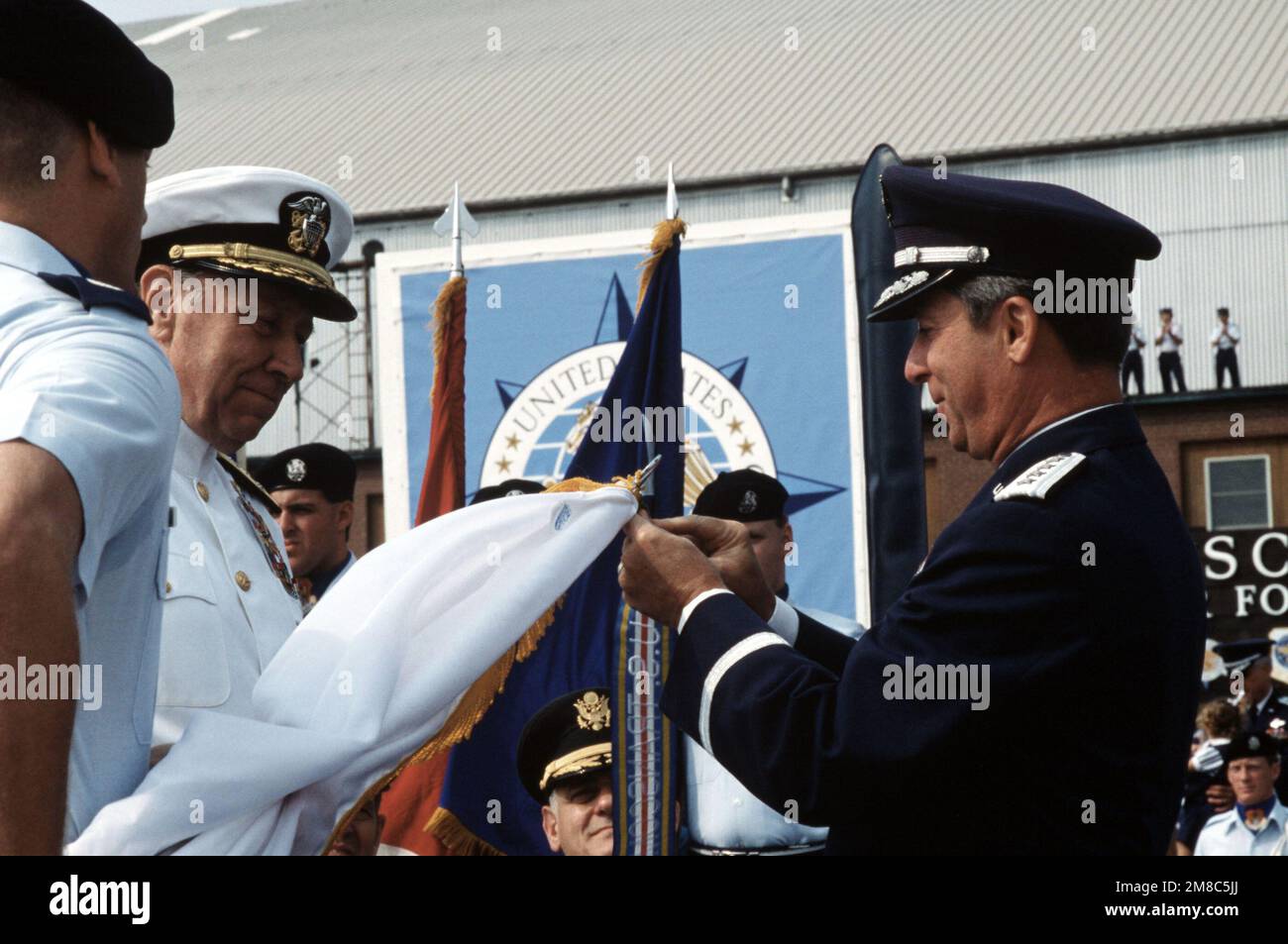 The chairman of the Joints Chiefs of STAFF, ADM William J. Crowe Jr., left, watches as GEN Duane H. Cassidy attaches a unit award to the flag of the U.S. Transportation Command (TRANSCOM). GEN Cassidy, who is retiring after 36 years of service, will be relieved as Commander in CHIEF, Military Airlift Command/TRANSCOM, by GEN Hansford T. Johnson. Base: Scott Air Force Base State: Illinois (IL) Country: United States Of America (USA) Stock Photo