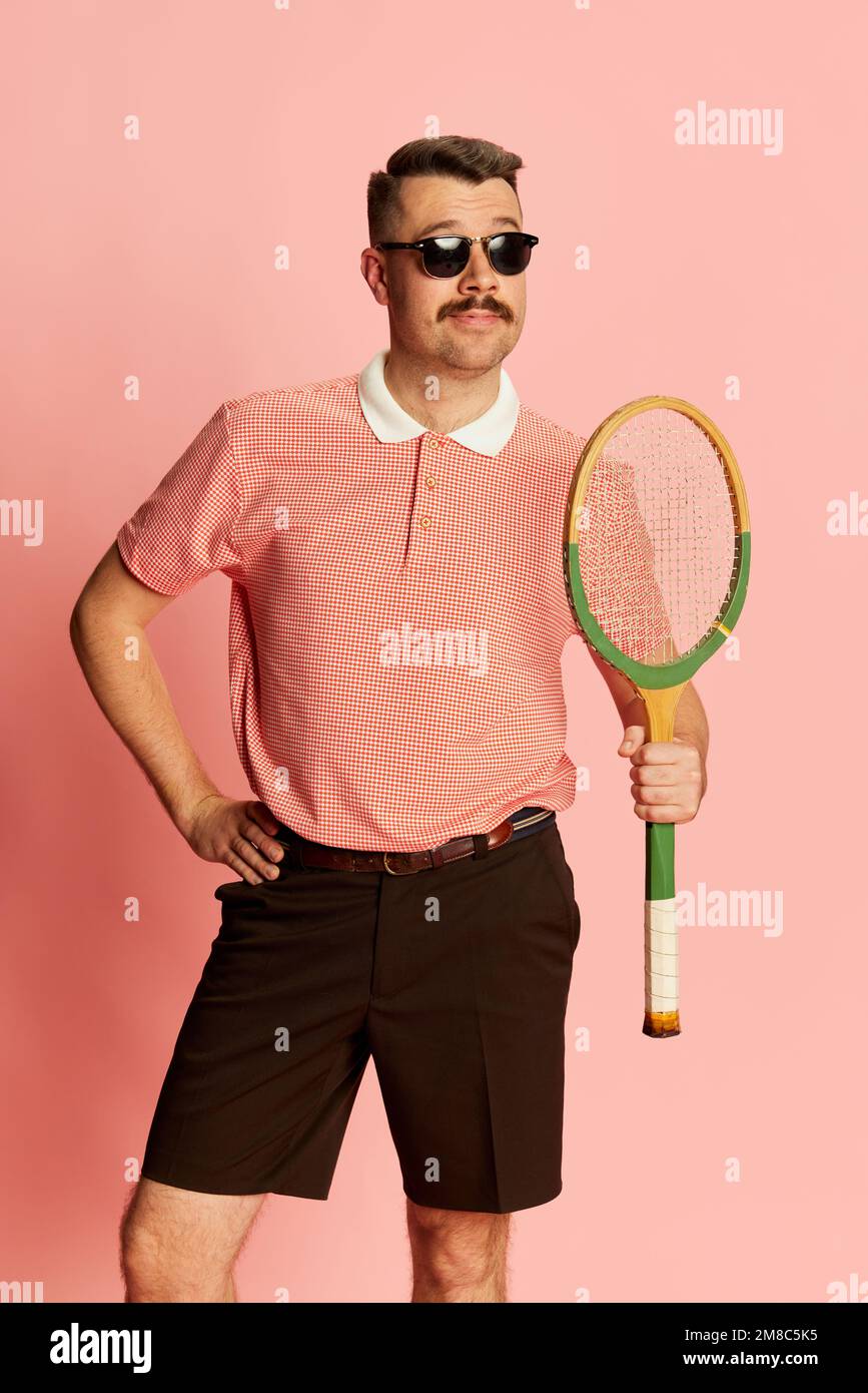 Joyful. Portraits of handsome charismatic man in stylish clothes posing with tennis racket over pink studio background. Concept of fashion, sport Stock Photo