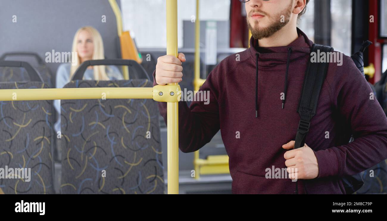 Close up of young man with beard wearing khudi, standing on bus, holding backpack, looking forward. Adult brunette traveling by public transport, busy. Concept of urban life. Stock Photo