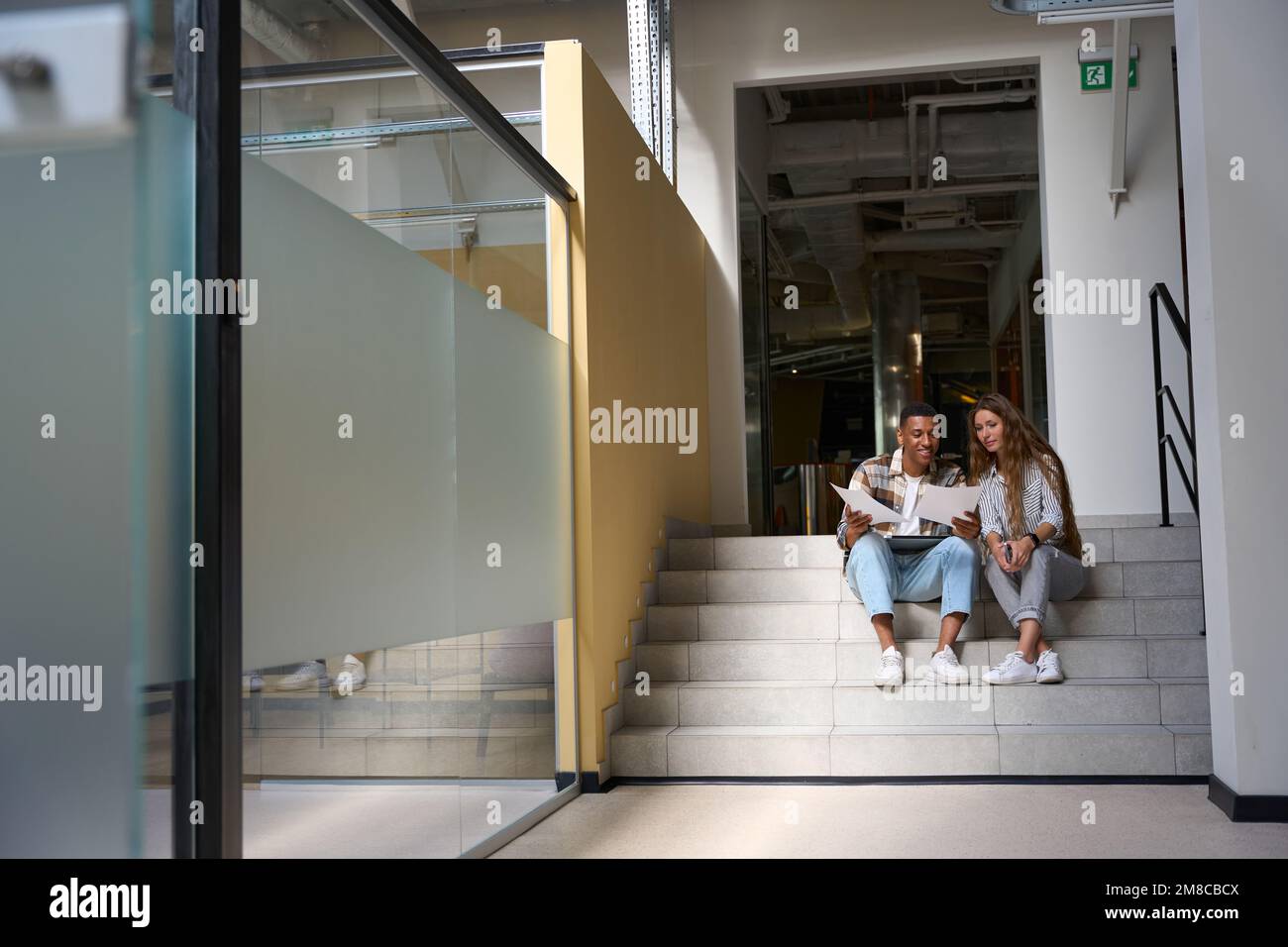 Smiling man and lady sitting on steps and examining the documents Stock Photo