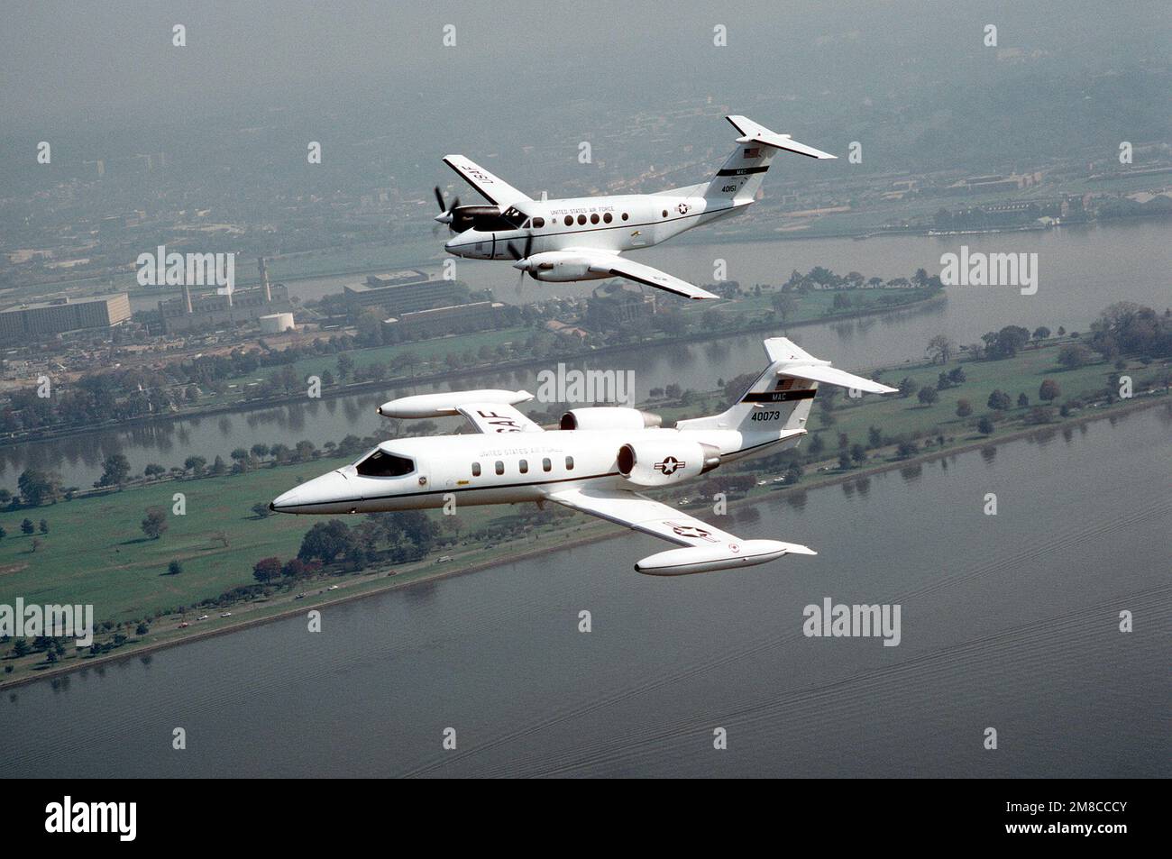 An air-to-air left side view of a C-21 aircraft and a C-12 Huron aircraft, both of the 1402nd Military Airlift Squadron. The planes are in flight over the Potomac River at Hains Point. Base: Washington State: District Of Columbia (DC) Country: United States Of America (USA) Stock Photo