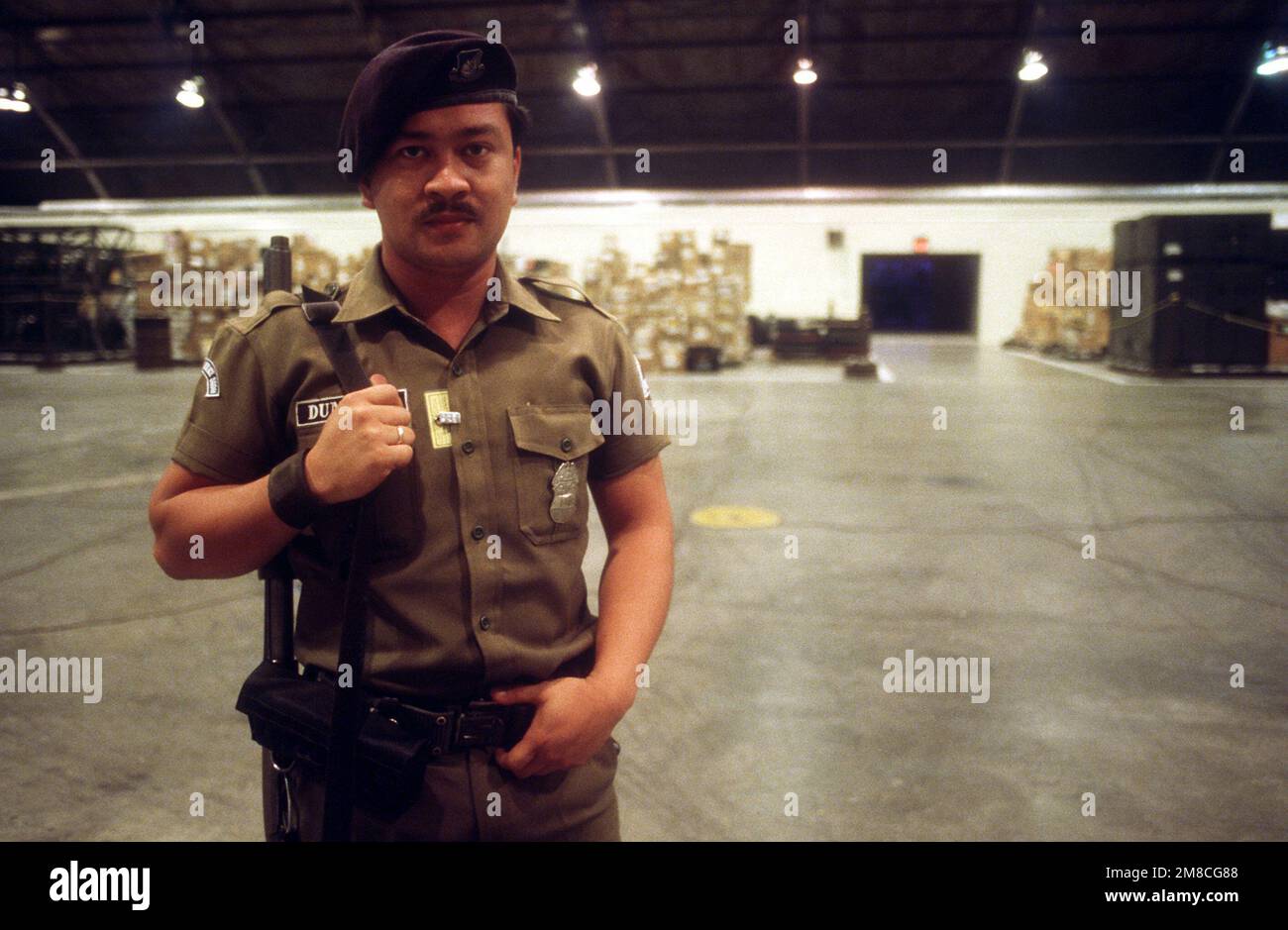 Michael Dunlop, a Filipino guard assigned to the base for exercise COPE THUNDER 89-5, stands watch in a maintenance hangar used for storing supplies and aircraft parts. Subject Operation/Series: COPE THUNDER 89-5 Base: Clark Air Base State: Luzon Country: Philippines (PHL) Stock Photo