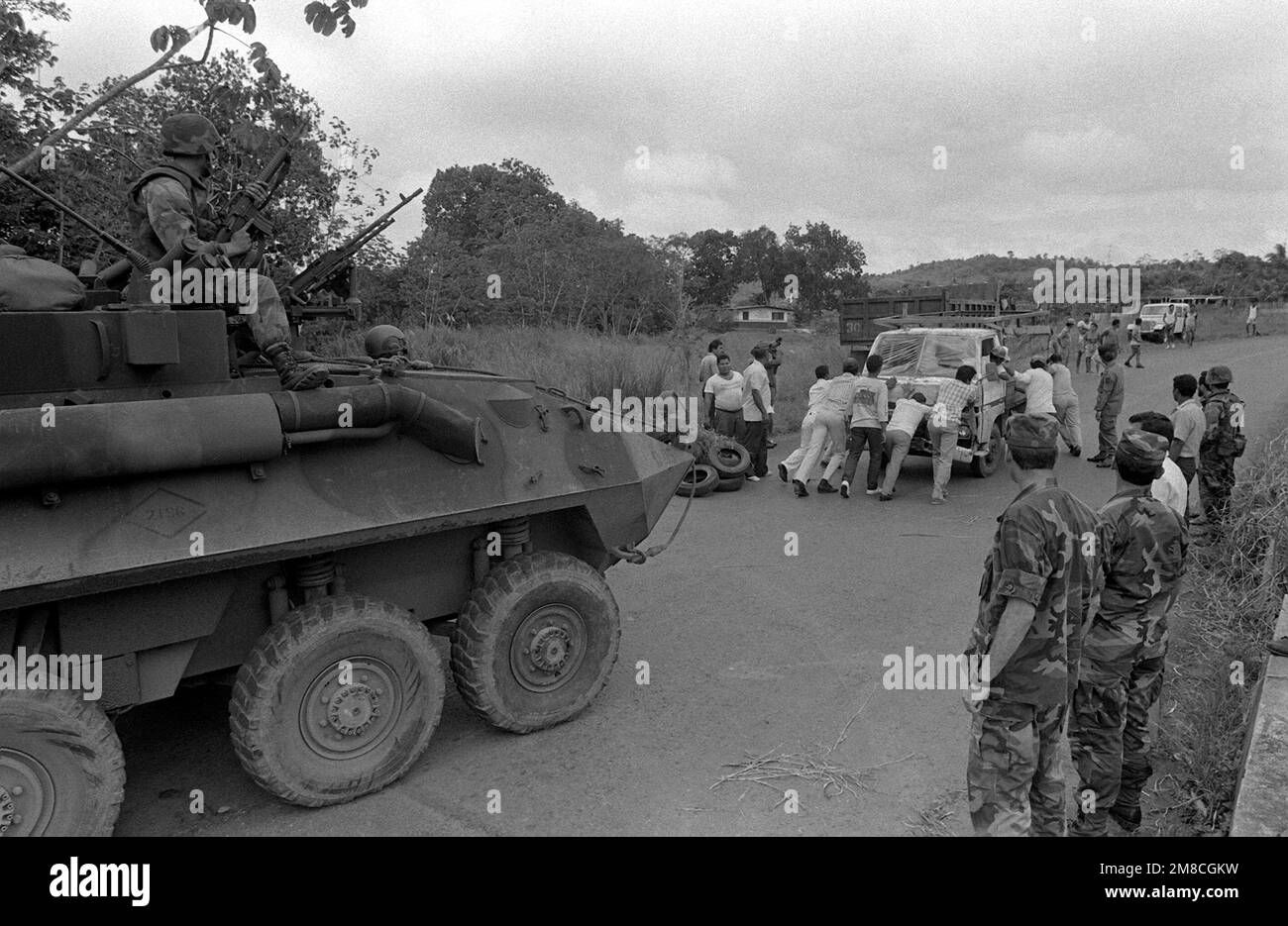 During Operation ROUGH RIDER, a route reconnaissance patrol, Marines from Company D, 2nd Light Armored Infantry Battalion, watch from atop their LAV25 light armored vehicle (LAV) as several Panamanians push a truck out of the road. The Panamanians, who had set up a road block to prevent the patrol from entering the town, agreed to move the vehicle after the Marines informed them that an LAV would be used to move it. Base: La Chorrera Country: Panama (PAN) Stock Photo