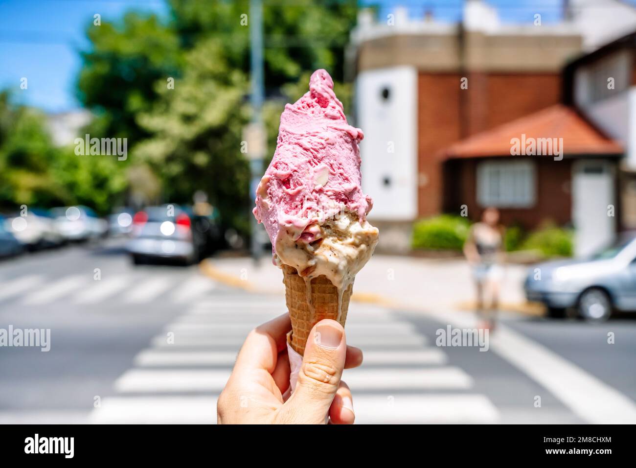 Ice cream in hand. Waffle cone with ice cream on the background of the street in the summer on a hot day. Street food, sweets, desserts concept. High quality photo Stock Photo