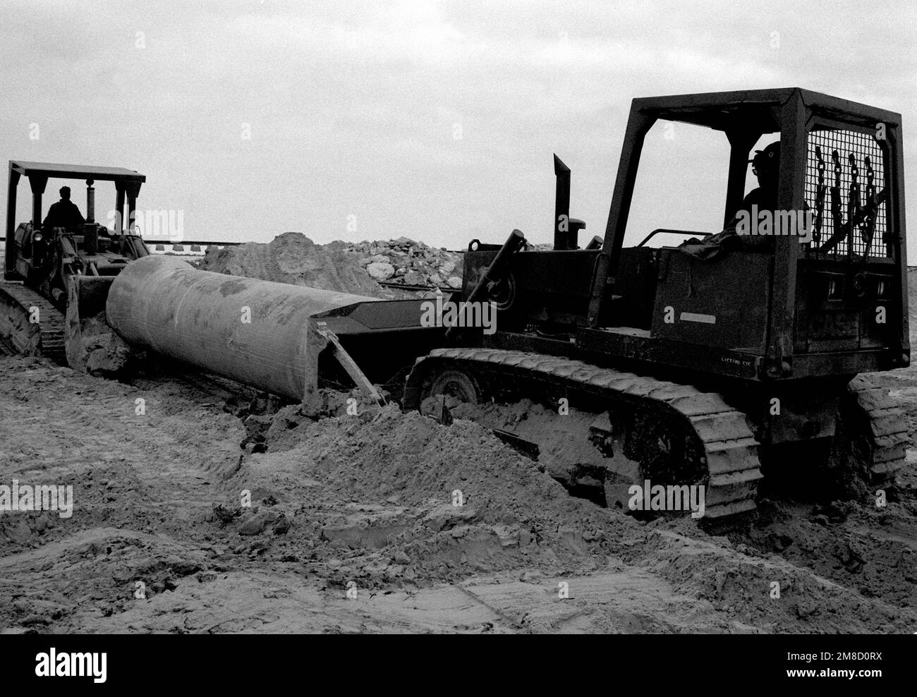 A US Navy Seabees use crawler tractors to move a cement culvert as they
