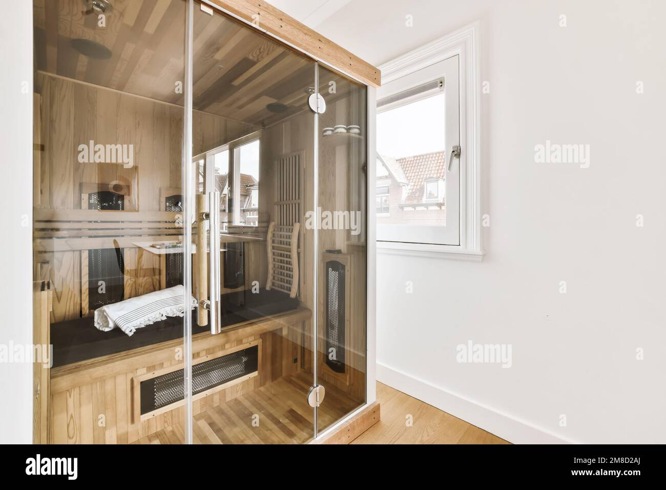 a bathroom with wooden floors and white walls, there is a glass shower stall in the corner to the right Stock Photo