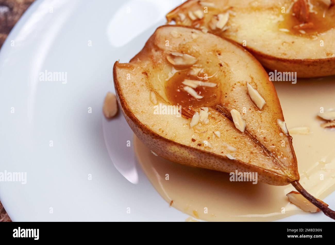 Honey baked pears with almonds, cinnamon, spices with sauce on white plate. Stock Photo