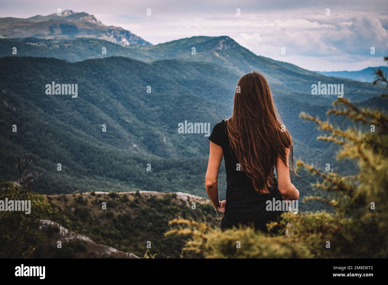 A back view of a female with long dark hair standing on highlands, with ...