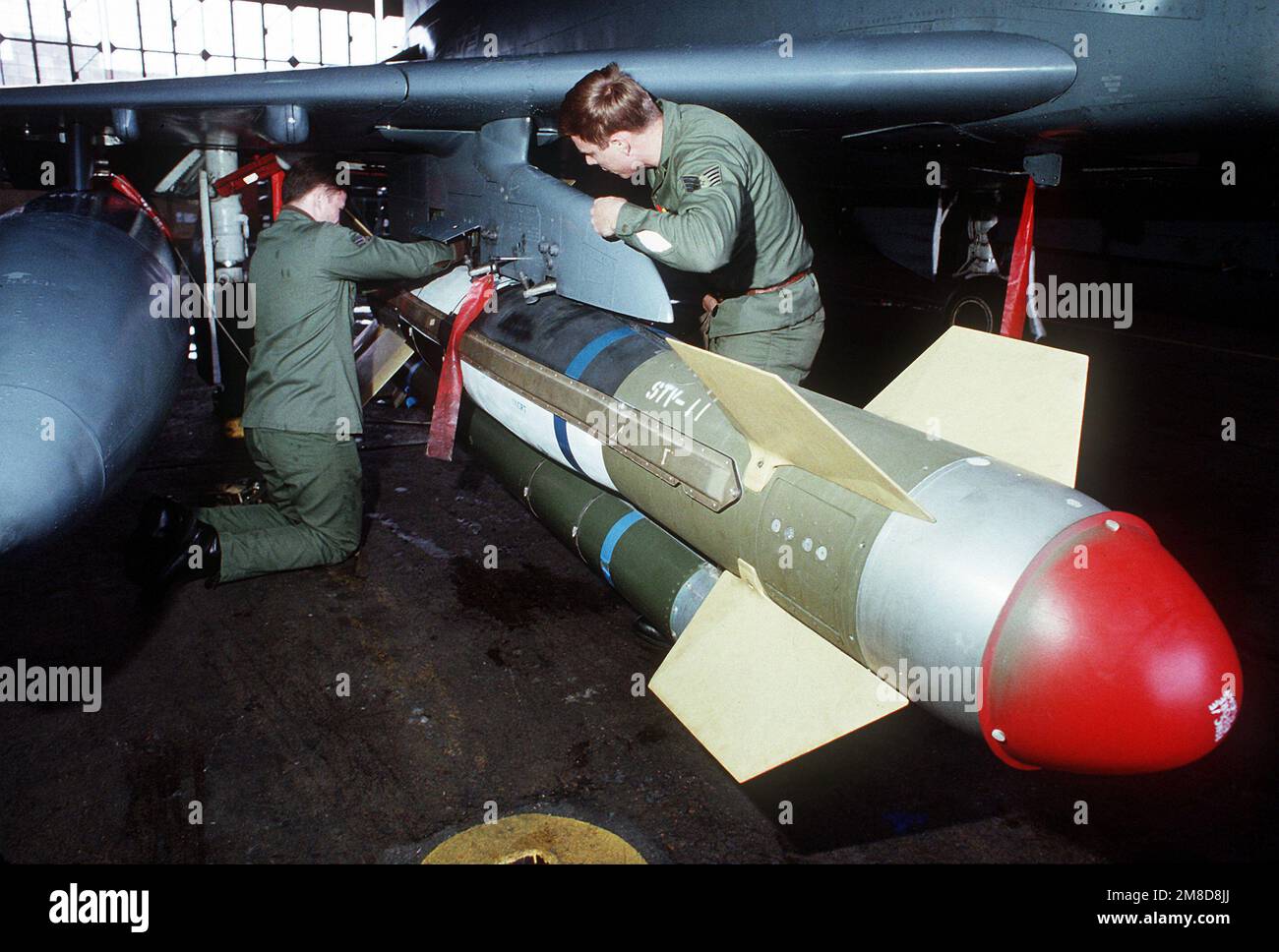 Ordnancemen attach a GBU-15 glide bomb to a pylon under the wing of an aircraft. Country: Unknown Stock Photo
