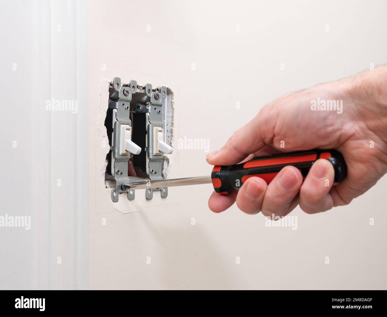 Male electrician repairing wall light switch panel. Handyman using screwdriver to install screw on light switch. Stock Photo