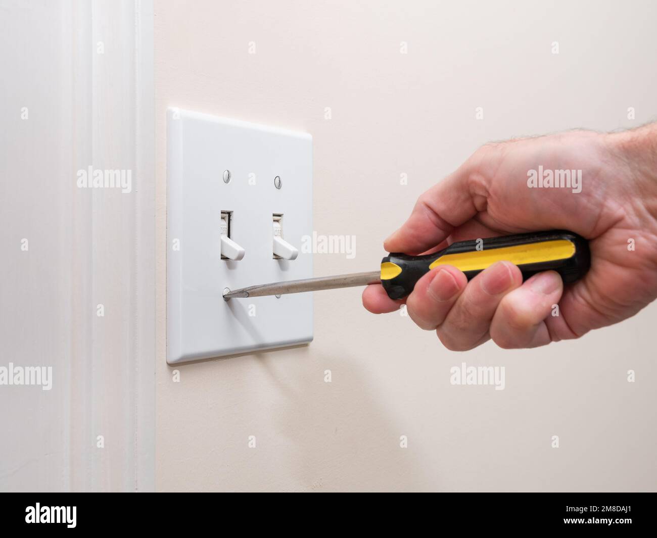 Male electrician repairing wall light switch panel. Handyman using screwdriver to install screw on light switch. Stock Photo