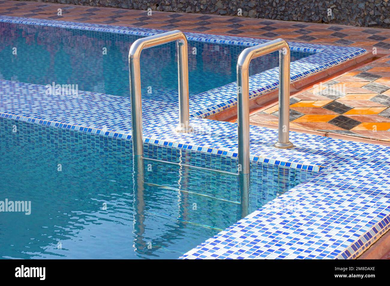 A metal swimming pool safe ladder (skimmer) on the entrance to the home inground poolside with the blue clean water. Stock Photo
