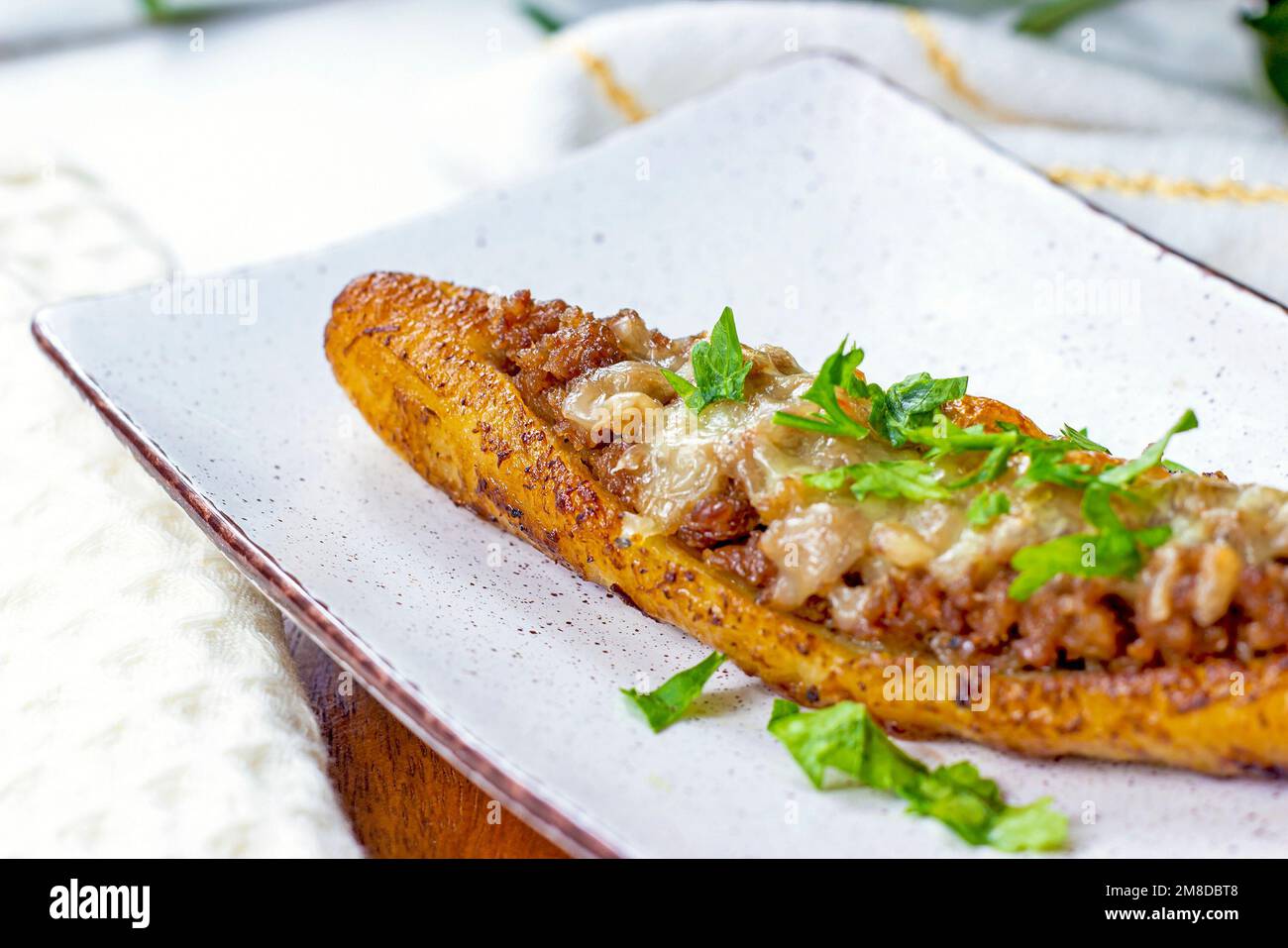 Baked Sweet Ripe Plantain Canoe (Canoas de Platanos Maduros) stuffed with ground meat, cheese and greens on a plate on wooden background. Stock Photo