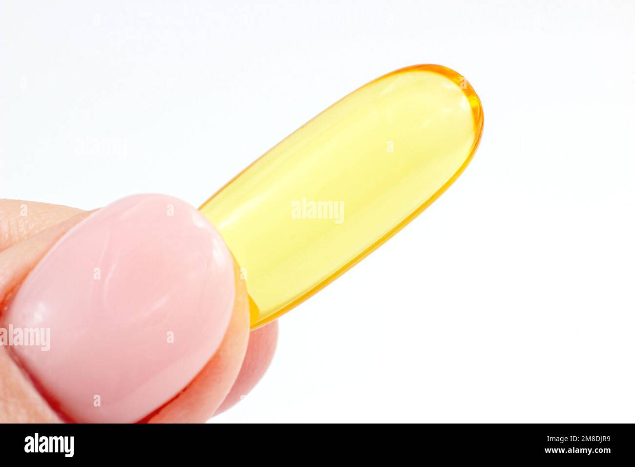 One omega-3 capsule (fish oil pill) in the woman hand close up with copy space on white background. Stock Photo