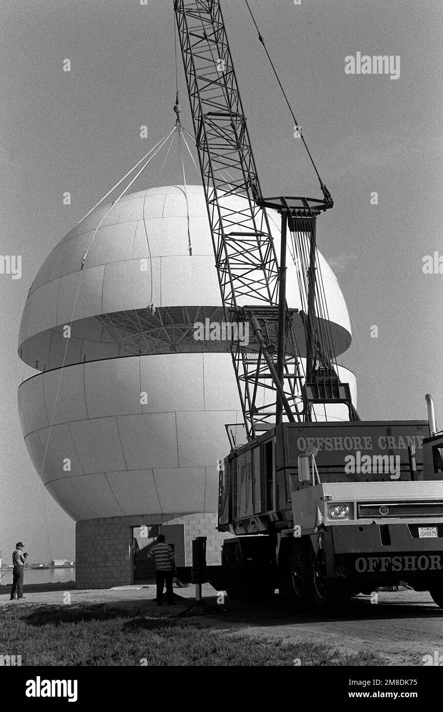 A crane is used to lower the upper half of a radome enclosure into place over a telemetry antenna. The polyurethane and fiberglass enclosure will protect the antenna from environmental damage while only slightly decreasing its receiving capabilities. Base: Pcfc Mssle Tst Cntr, Point Magu State: California (CA) Country: United States Of America (USA) Stock Photo
