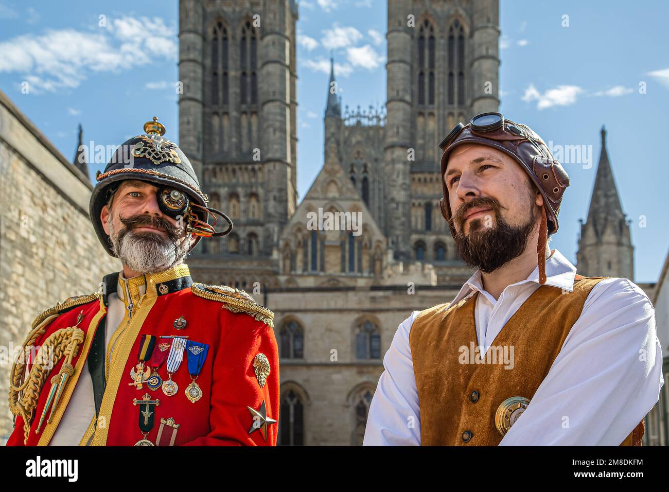Two male steampunks with Lincoln Cathedral in the background. Military, explorer, pilot, adventurer themed steampunk costumes. Stock Photo
