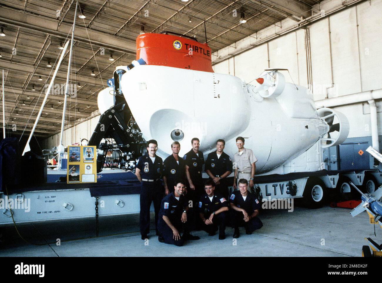 The crew of the U.S. Navy deep submergence vehicle TURTLE (DSV 3) stands in front of the craft as it sits on its trailer in a hangar at the air station. The TURTLE has been conducting sea trails with its support ship, the civilian vessel DOLORES CHOUEST. Base: Naval Air Station, North Island State: California(CA) Country: United States Of America (USA) Stock Photo