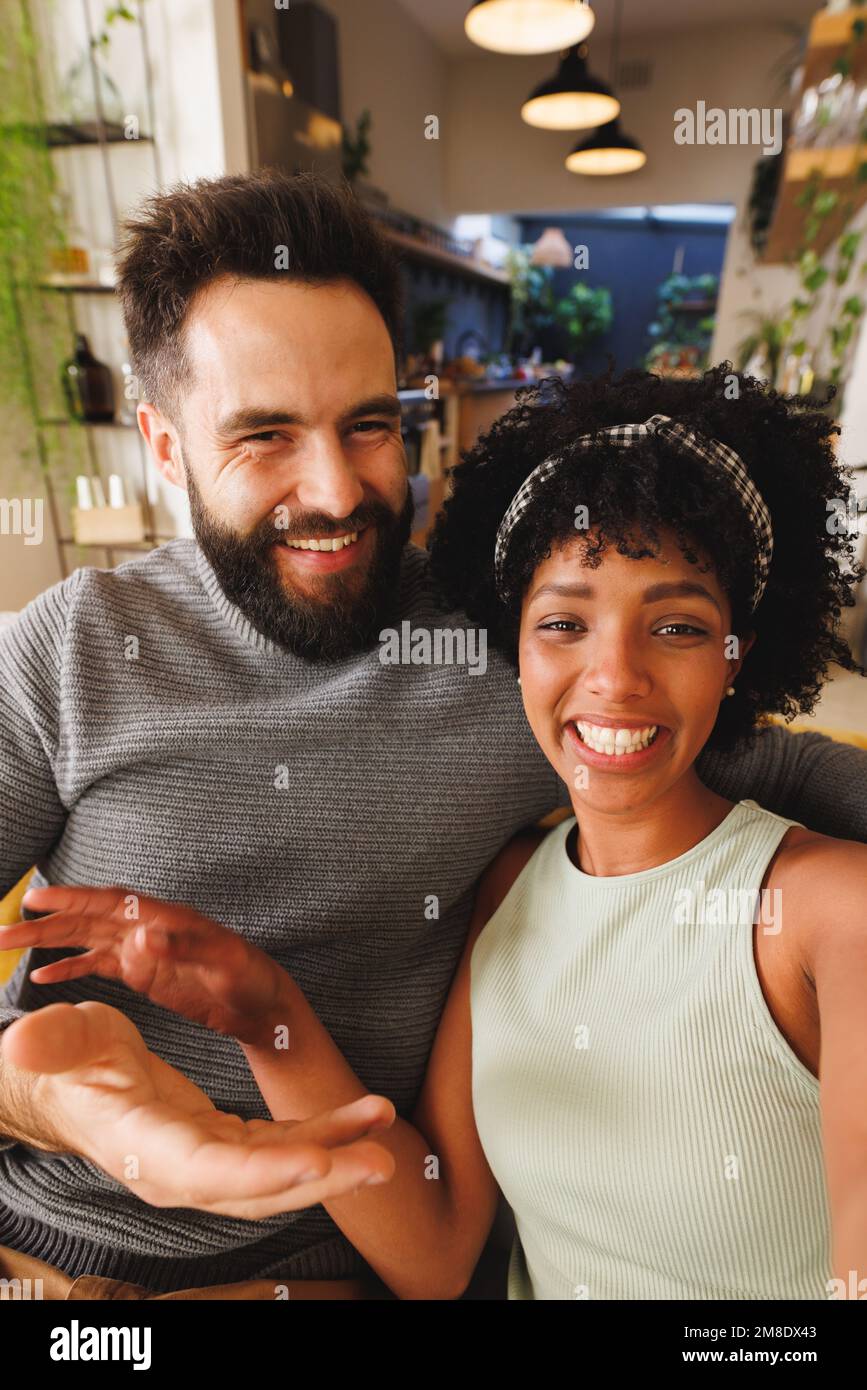 Portrait of cheerful biracial young couple smiling while relaxing on sofa in living room Stock Photo