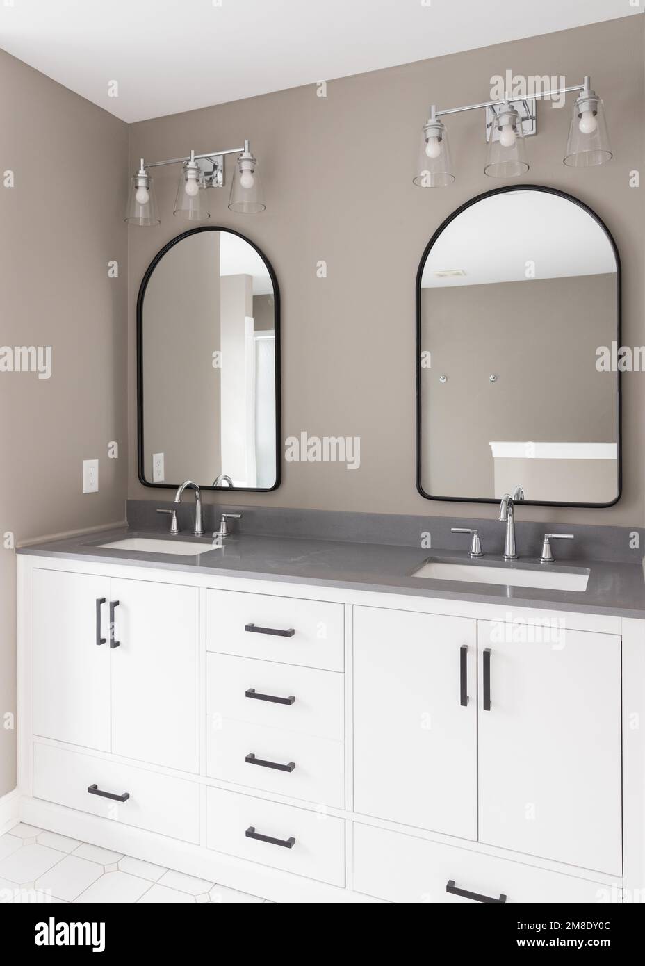 A bathroom with a white vanity and black hardware, chrome faucets on a  quartz countertop, arched mirrors, and brown walls Stock Photo - Alamy