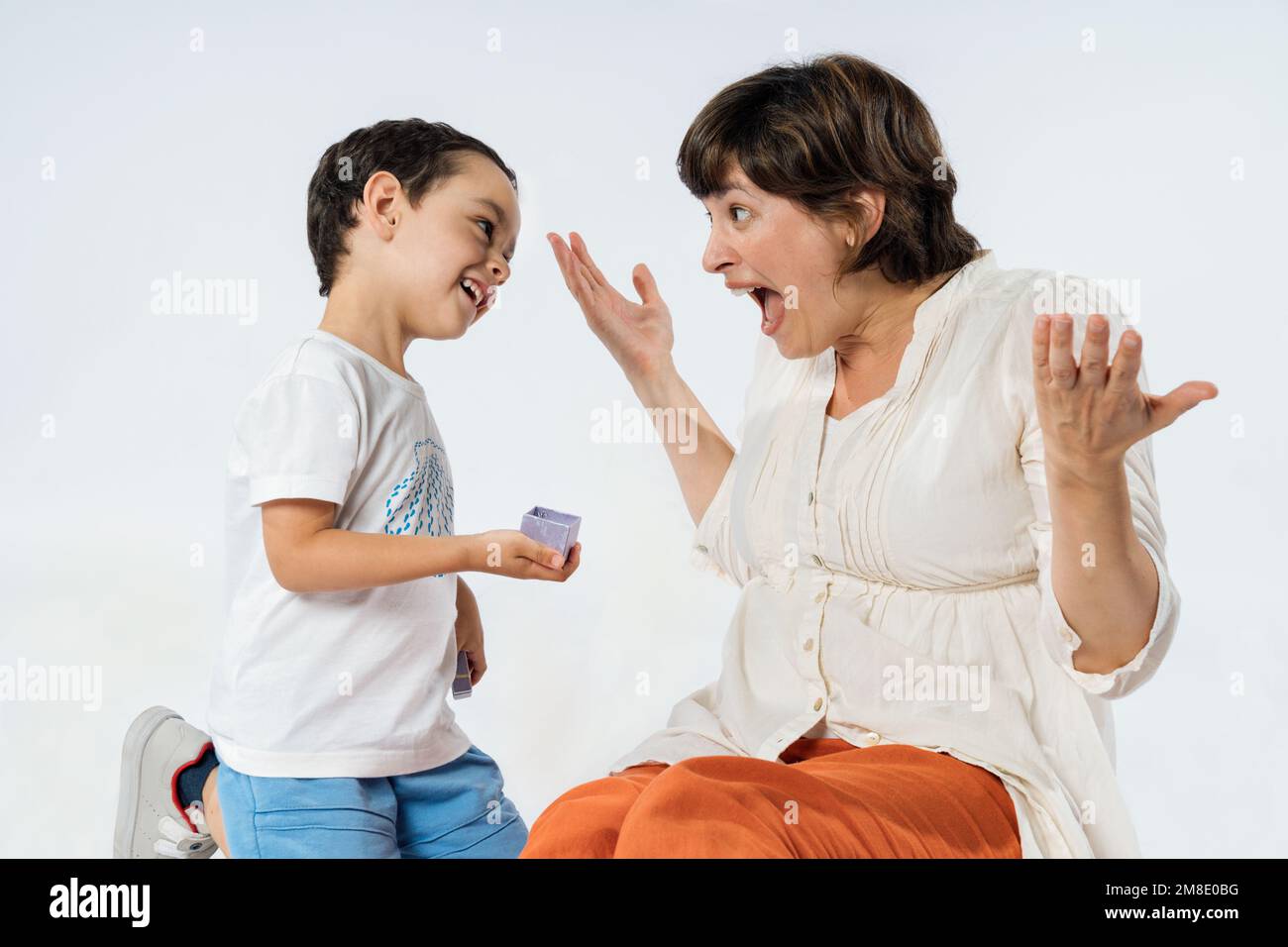 A little boy surprises his mother with a gift. Mother's day concept. Studio image with white background. Stock Photo