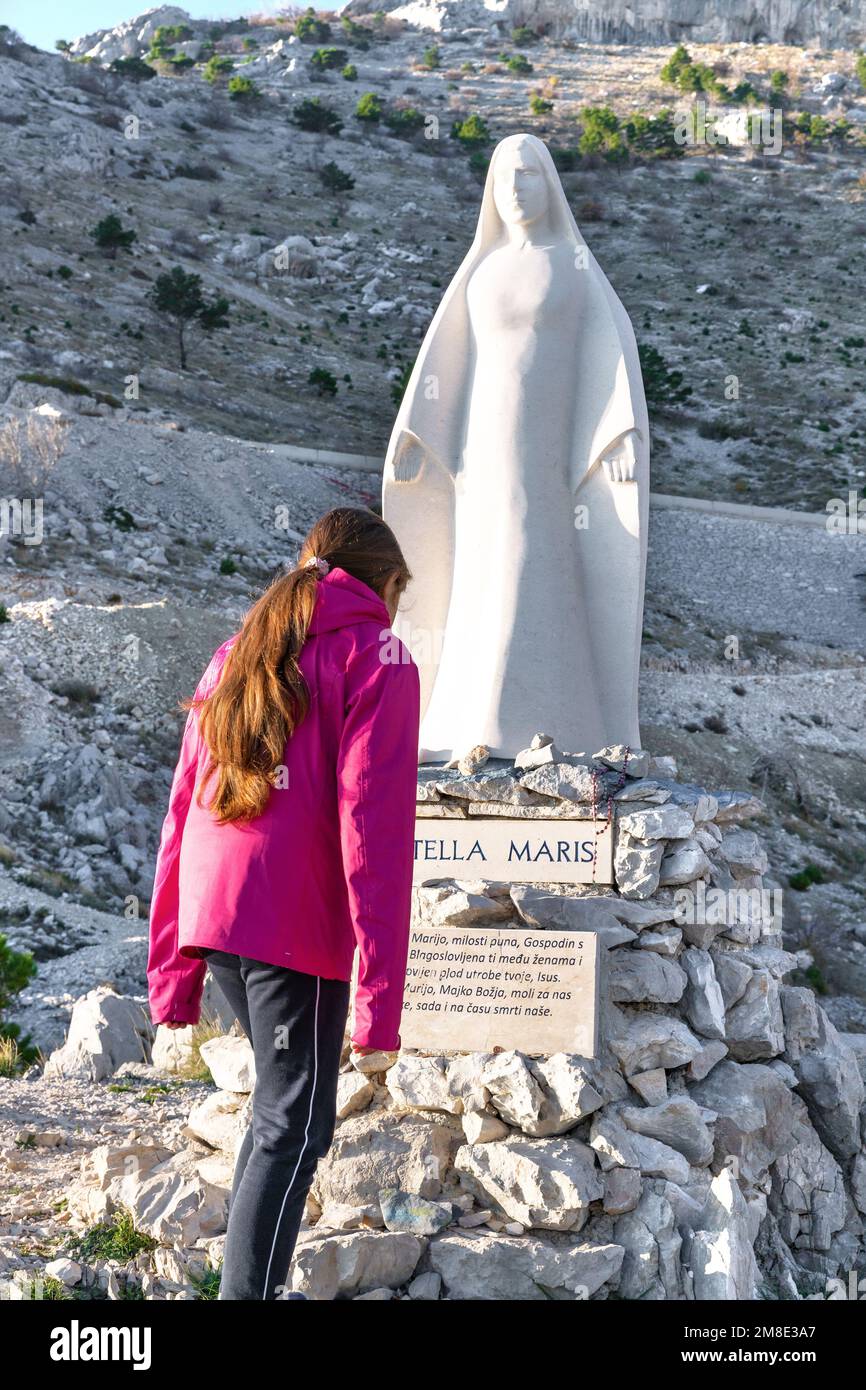 Stella Maris viewpoint and sculpture. Girl  prays near the Stella Maris (The Star of the Sea). Jesus' mother sculpture above the sea in Croatia. Stock Photo