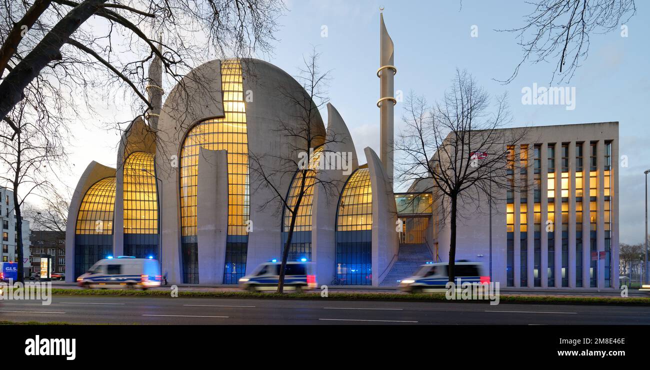 Cologne, Germany, January 11, 2023:  fast police cars with with motion blur and blue lights flashing at illuminated cologne central mosque at dusk Stock Photo