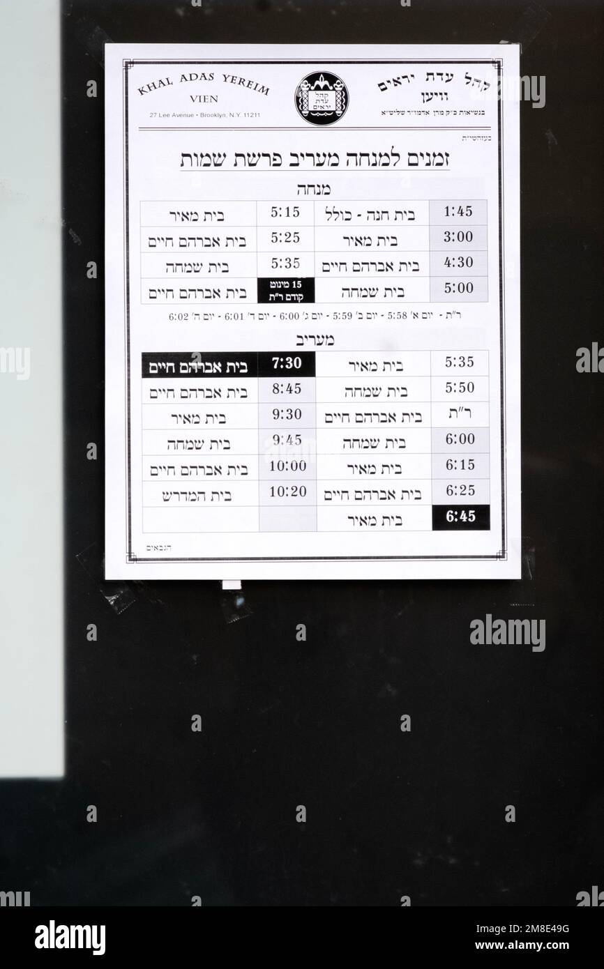 A sign outside a hasidic synagogue listing the times for afternoon and evening prayer services for the upcoming week. In Brooklyn, New York. Stock Photo
