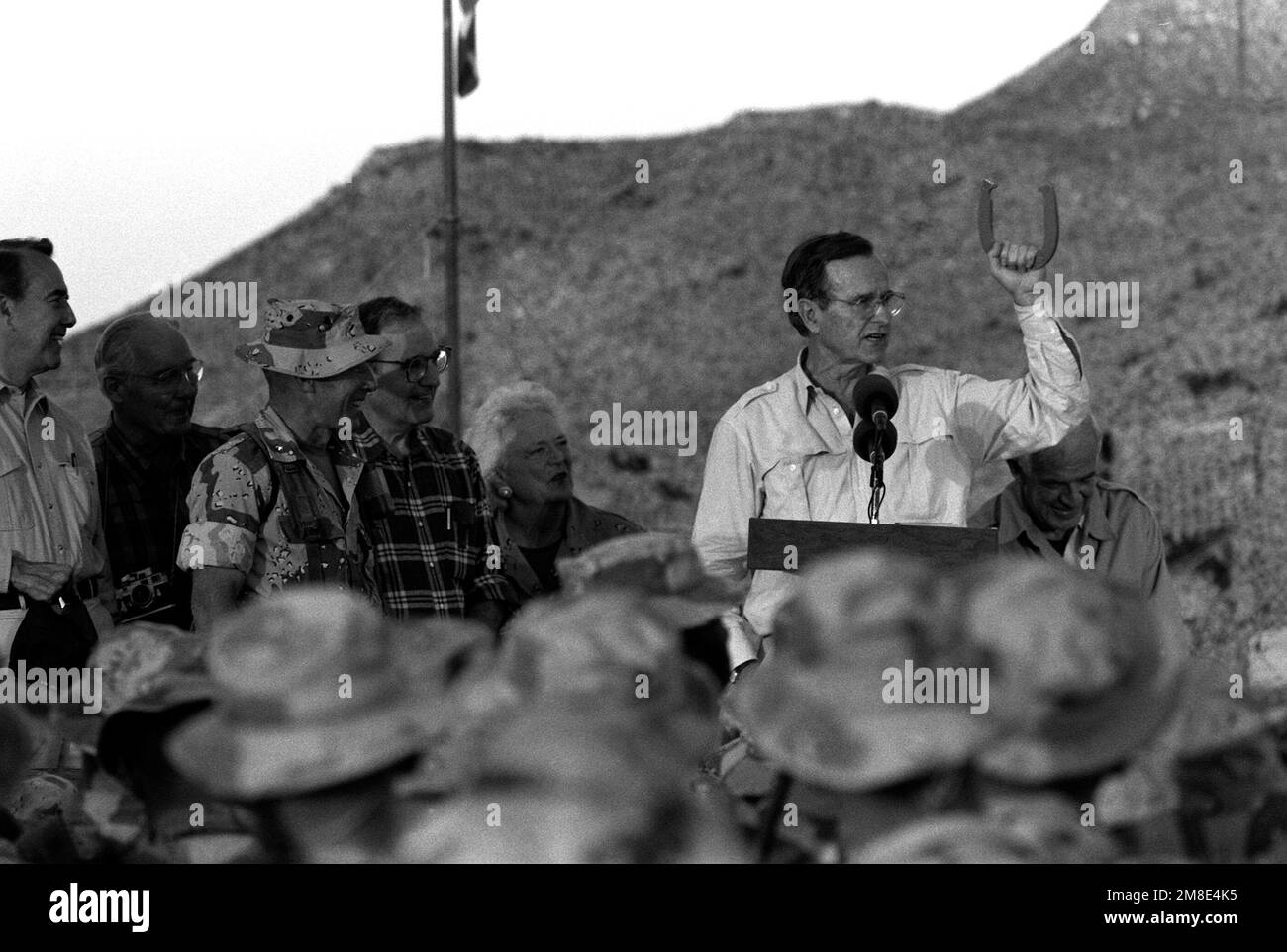 With his wife, Barbara, beside him, President George Bush holds up a horseshoe as he speaks from the back of a truck during his Thanksgiving Day visit to the lst Marine Division combat operations center (COC) during Operation Desert Shield. Also on the truck are Sen. Robert Dole, left, and Speaker of the House Tom Foley, right.. Subject Operation/Series: DESERT SHIELD Country: Saudi Arabia(SAU) Stock Photo