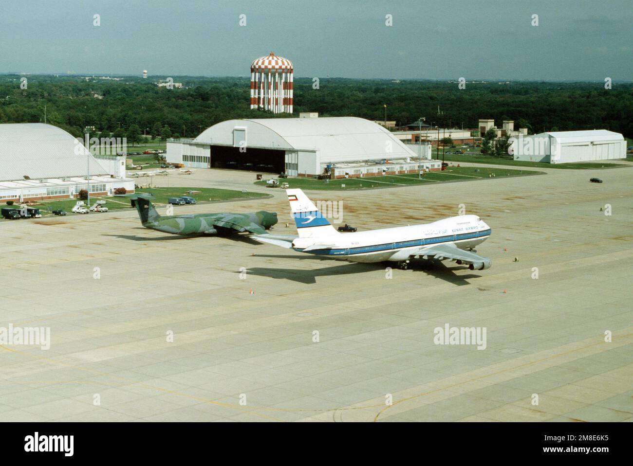 A Boeing 747 commercial aircraft of Kuwait Airways stands on the flight line beside a C141B