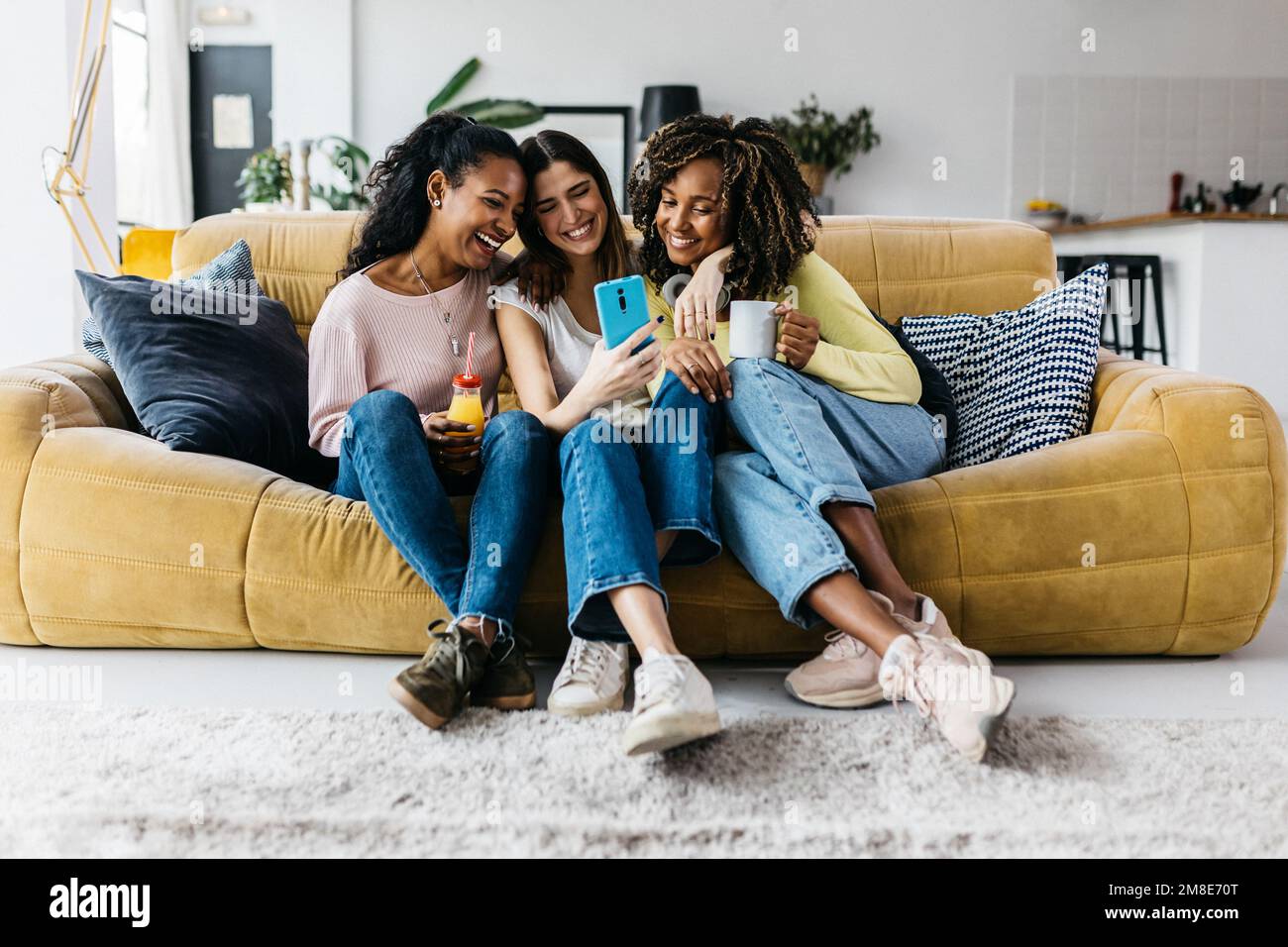 Three happy multiracial young women friends having fun using mobile phone Stock Photo