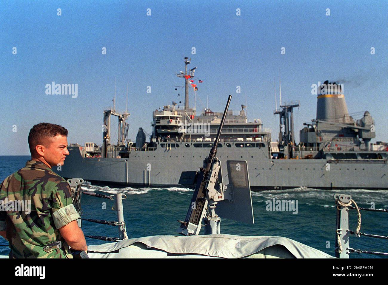 A Marine stands near a pedestal-mounted M-2 .50-caliber machine gun aboard the battleship USS WISCONSIN (BB-64) as the combat stores ship USNS SPICE (T-AFS-9) steams alongside during a vertical replenishment operation. The ships are part of the U.S. Navy force in the gulf supporting Operation Desert Shield. Subject Operation/Series: DESERT SHIELD Country: Unknown Stock Photo