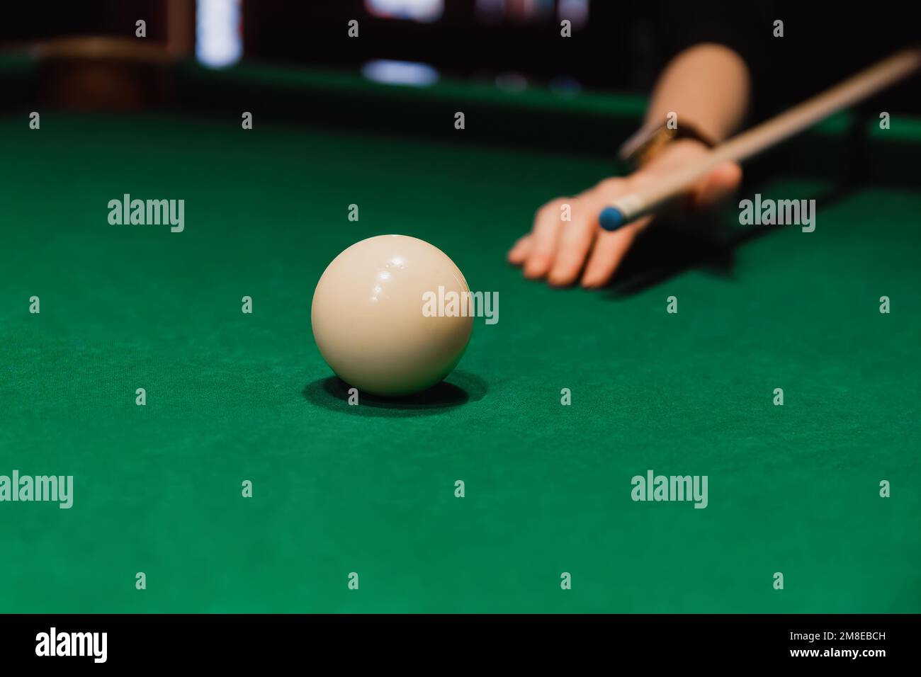 Player holding que and aiming to billiard white ball. White ball on gree poll table Stock Photo